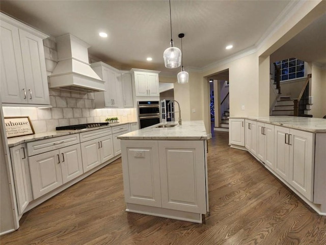 kitchen with hanging light fixtures, black gas stovetop, an island with sink, and white cabinets