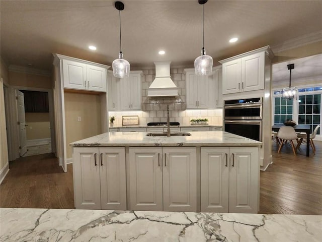 kitchen with pendant lighting, white cabinetry, stainless steel appliances, light stone countertops, and custom range hood