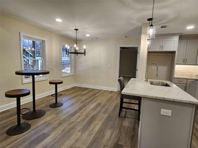 kitchen with an island with sink, sink, gray cabinetry, hanging light fixtures, and light stone counters