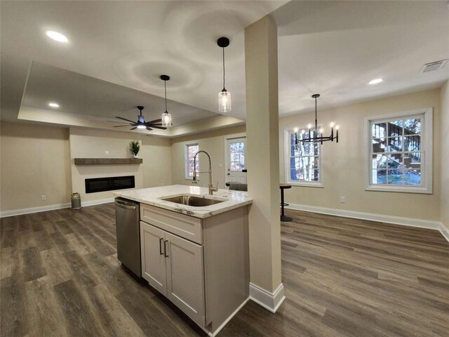 kitchen featuring sink, dark wood-type flooring, light stone countertops, decorative light fixtures, and a raised ceiling