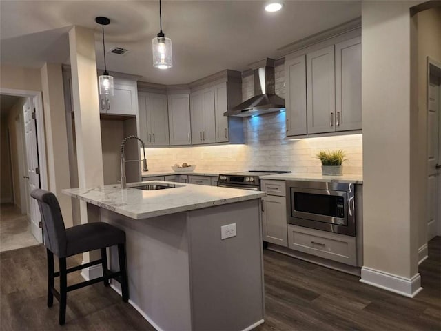 kitchen with sink, stainless steel microwave, an island with sink, light stone countertops, and wall chimney range hood