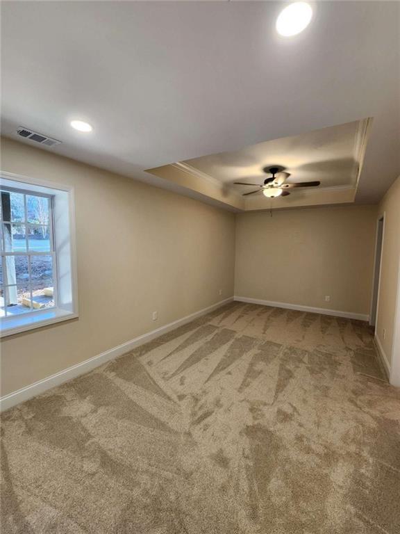 carpeted empty room with ceiling fan and a raised ceiling