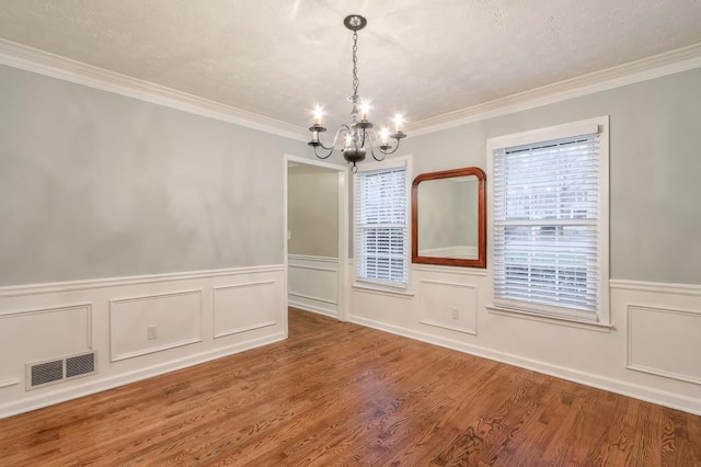 spare room featuring wood-type flooring, ornamental molding, a textured ceiling, and an inviting chandelier