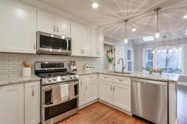 kitchen featuring white cabinetry, sink, hanging light fixtures, stainless steel appliances, and light wood-type flooring