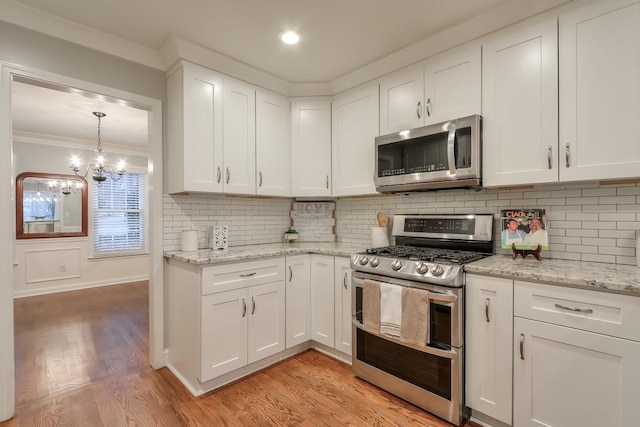 kitchen with stainless steel appliances, crown molding, white cabinets, and light hardwood / wood-style floors