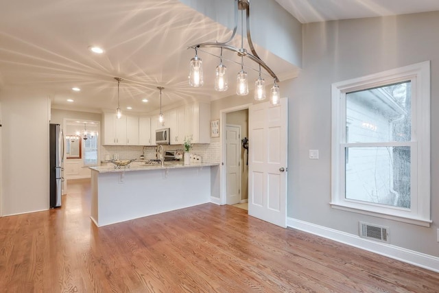 kitchen featuring appliances with stainless steel finishes, hanging light fixtures, light stone countertops, white cabinets, and kitchen peninsula