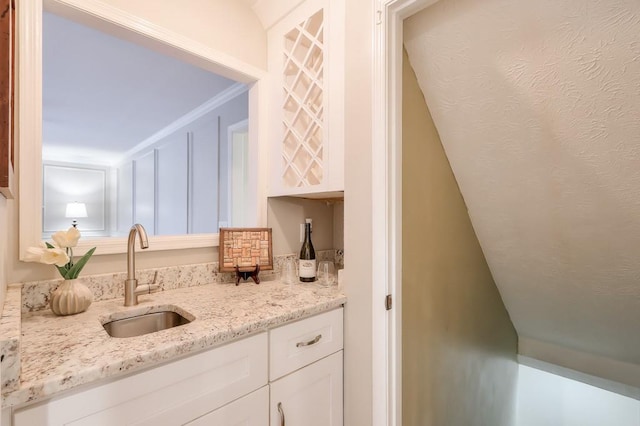 kitchen with white cabinetry, light stone countertops, sink, and crown molding