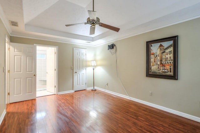 unfurnished bedroom featuring crown molding, a tray ceiling, ensuite bath, and hardwood / wood-style flooring