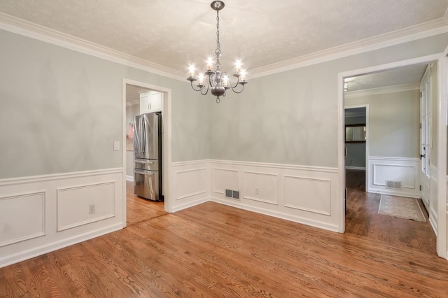 unfurnished room featuring a notable chandelier, ornamental molding, and light wood-type flooring