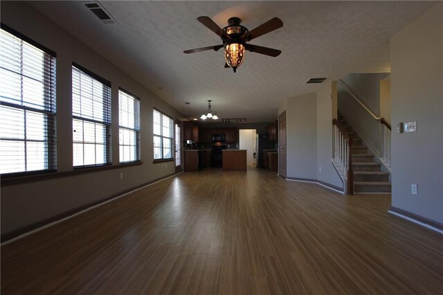 unfurnished living room featuring visible vents, stairs, a textured ceiling, light wood-type flooring, and ceiling fan with notable chandelier