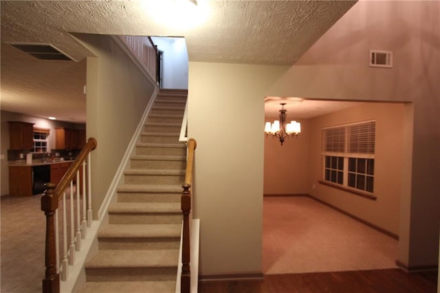 stairway with a chandelier, visible vents, a textured ceiling, and baseboards