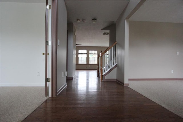 hall featuring stairs, baseboards, dark carpet, and dark wood-style flooring