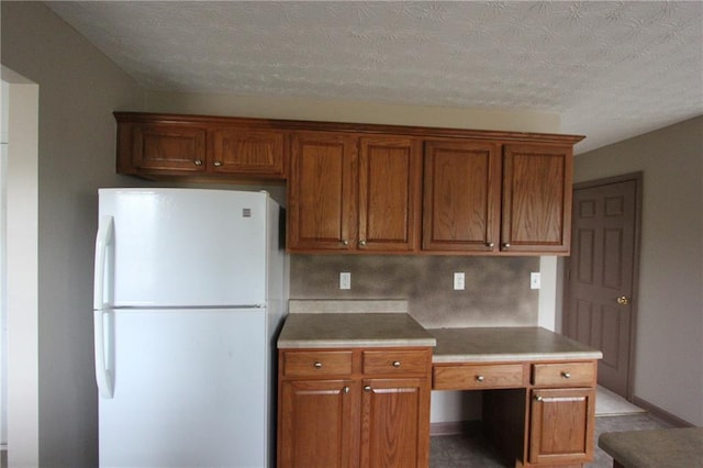 kitchen featuring a textured ceiling, light countertops, freestanding refrigerator, and brown cabinets