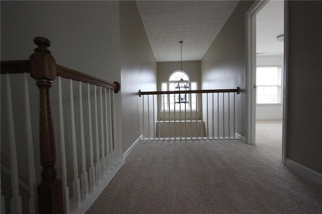 hallway featuring a notable chandelier, carpet floors, and baseboards