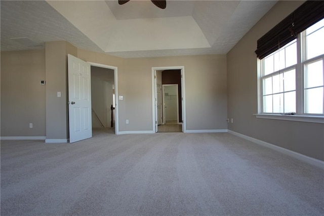 unfurnished bedroom featuring ensuite bathroom, baseboards, a raised ceiling, and light colored carpet