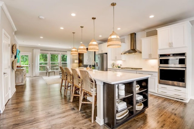 kitchen with pendant lighting, white cabinets, a spacious island, wall chimney exhaust hood, and stainless steel appliances