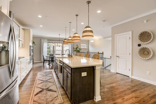 kitchen with hanging light fixtures, stainless steel appliances, crown molding, an island with sink, and dark brown cabinets