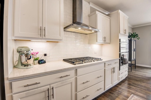 kitchen featuring appliances with stainless steel finishes, dark hardwood / wood-style flooring, light stone counters, wall chimney exhaust hood, and white cabinetry