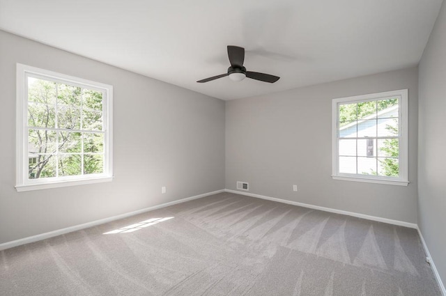 carpeted spare room with ceiling fan, plenty of natural light, visible vents, and baseboards