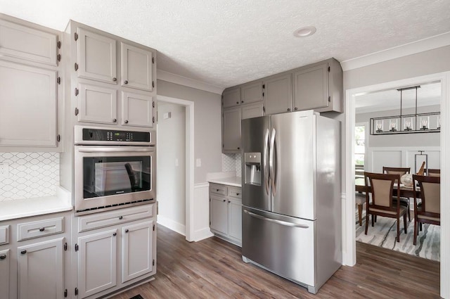 kitchen with appliances with stainless steel finishes, dark wood finished floors, crown molding, and gray cabinetry