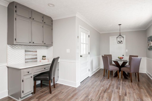 dining room featuring light wood-style flooring, crown molding, a textured ceiling, and wainscoting