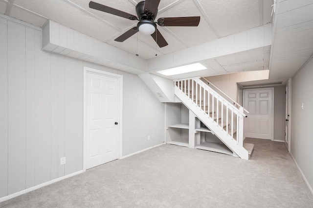 finished basement featuring carpet floors, stairway, baseboards, and a ceiling fan