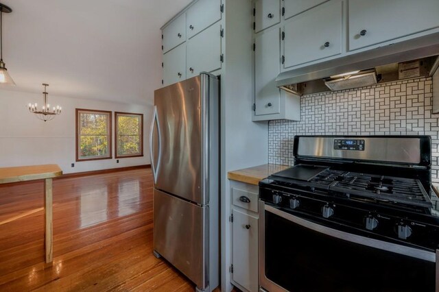 kitchen with hanging light fixtures, stainless steel appliances, backsplash, a chandelier, and light wood-type flooring