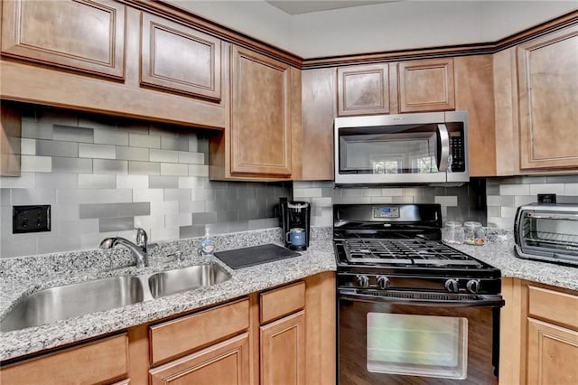 kitchen featuring decorative backsplash, gas stove, light stone countertops, and sink