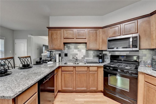 kitchen featuring black appliances, light stone countertops, light wood-type flooring, and sink