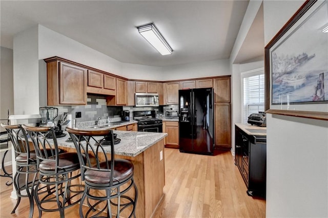 kitchen with decorative backsplash, light stone countertops, sink, black appliances, and light hardwood / wood-style flooring