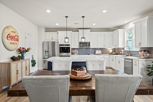 kitchen with a center island, appliances with stainless steel finishes, hanging light fixtures, sink, and light hardwood / wood-style flooring