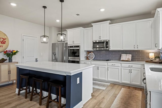 kitchen with light hardwood / wood-style floors, white cabinets, hanging light fixtures, a kitchen island, and appliances with stainless steel finishes