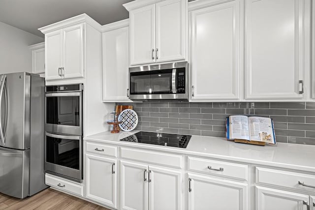 kitchen with light hardwood / wood-style floors, white cabinetry, backsplash, and appliances with stainless steel finishes