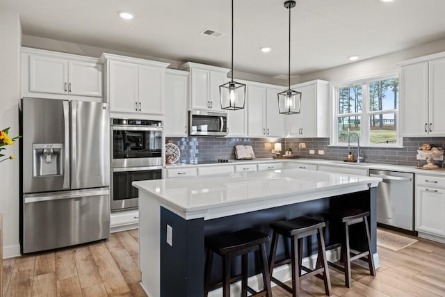 kitchen featuring stainless steel appliances, light hardwood / wood-style floors, a kitchen island, white cabinetry, and decorative light fixtures