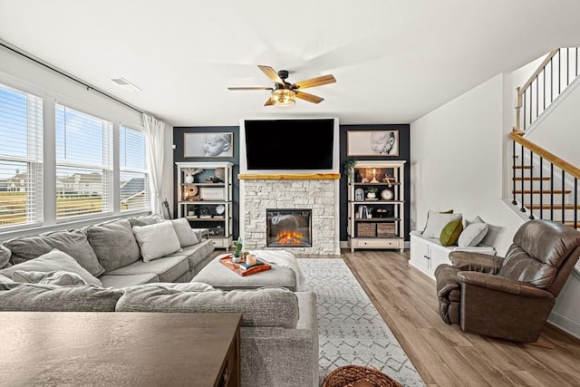 living room featuring a fireplace, ceiling fan, and light wood-type flooring