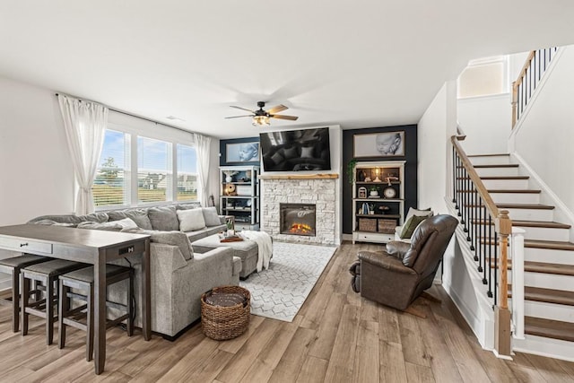 living room with ceiling fan, a stone fireplace, and light hardwood / wood-style flooring