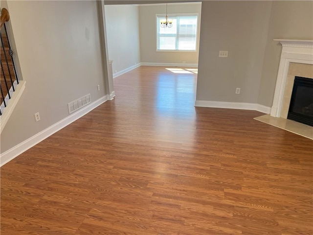 unfurnished living room with dark hardwood / wood-style floors, a premium fireplace, and a chandelier