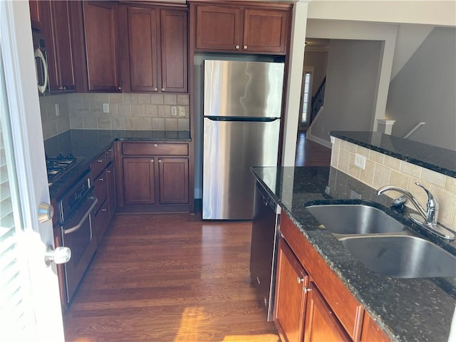 kitchen with dark wood-type flooring, sink, appliances with stainless steel finishes, dark stone counters, and decorative backsplash