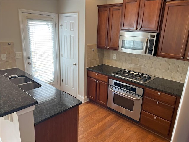 kitchen with appliances with stainless steel finishes, sink, light hardwood / wood-style flooring, and dark stone counters