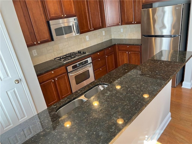 kitchen featuring sink, light wood-type flooring, appliances with stainless steel finishes, dark stone counters, and decorative backsplash