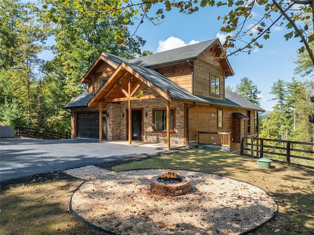 view of front of home featuring aphalt driveway, a fire pit, a garage, fence, and stone siding