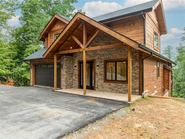 view of front of home with an attached garage, stone siding, driveway, and a patio area