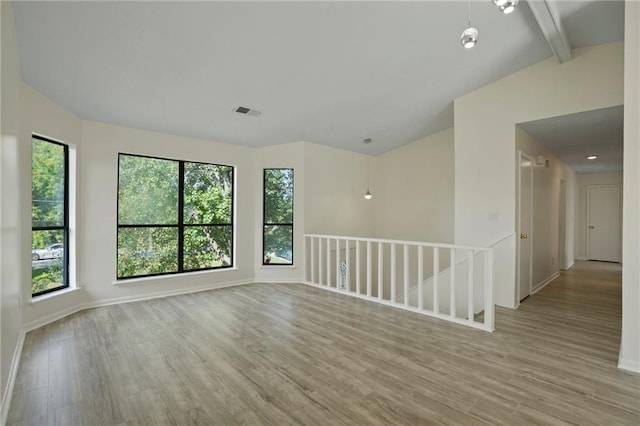 empty room with lofted ceiling with beams, a wealth of natural light, and light hardwood / wood-style flooring