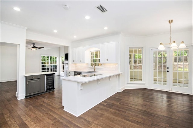 kitchen featuring wine cooler, light countertops, a peninsula, dark wood-style flooring, and ornamental molding