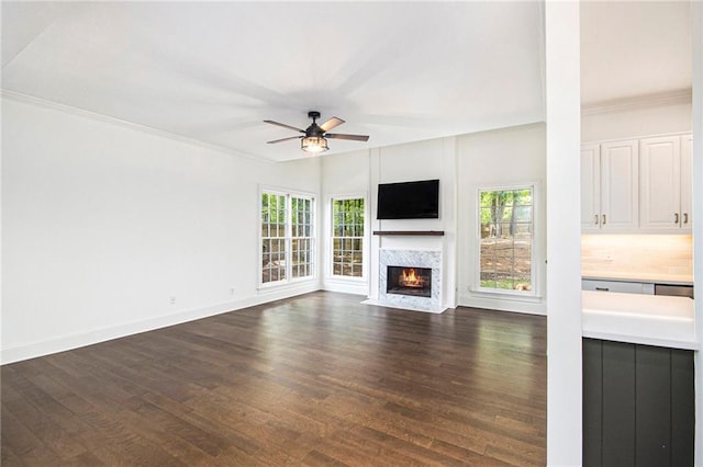 unfurnished living room with a ceiling fan, dark wood-style flooring, a fireplace with flush hearth, crown molding, and baseboards
