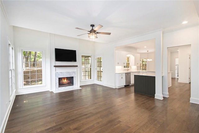 unfurnished living room with a ceiling fan, dark wood-style floors, a premium fireplace, baseboards, and a sink
