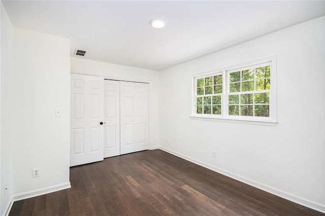 unfurnished bedroom featuring dark wood finished floors, baseboards, and a closet