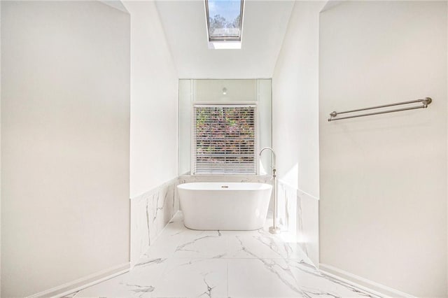 full bathroom featuring a soaking tub, marble finish flooring, and wainscoting