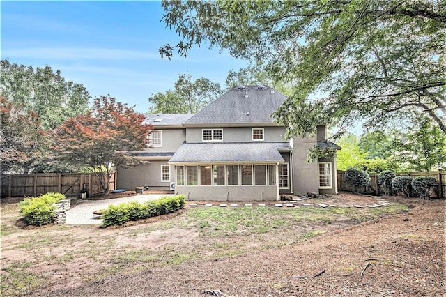 rear view of house featuring stucco siding, a sunroom, a fenced backyard, a patio area, and a gate