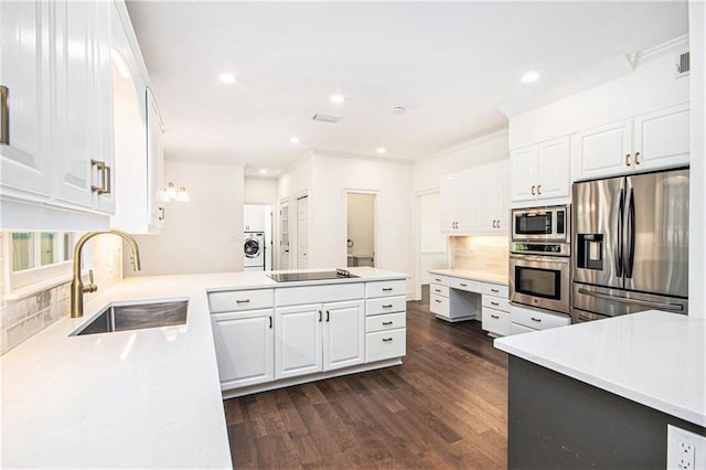 kitchen with appliances with stainless steel finishes, a sink, washer / clothes dryer, a peninsula, and dark wood-style flooring